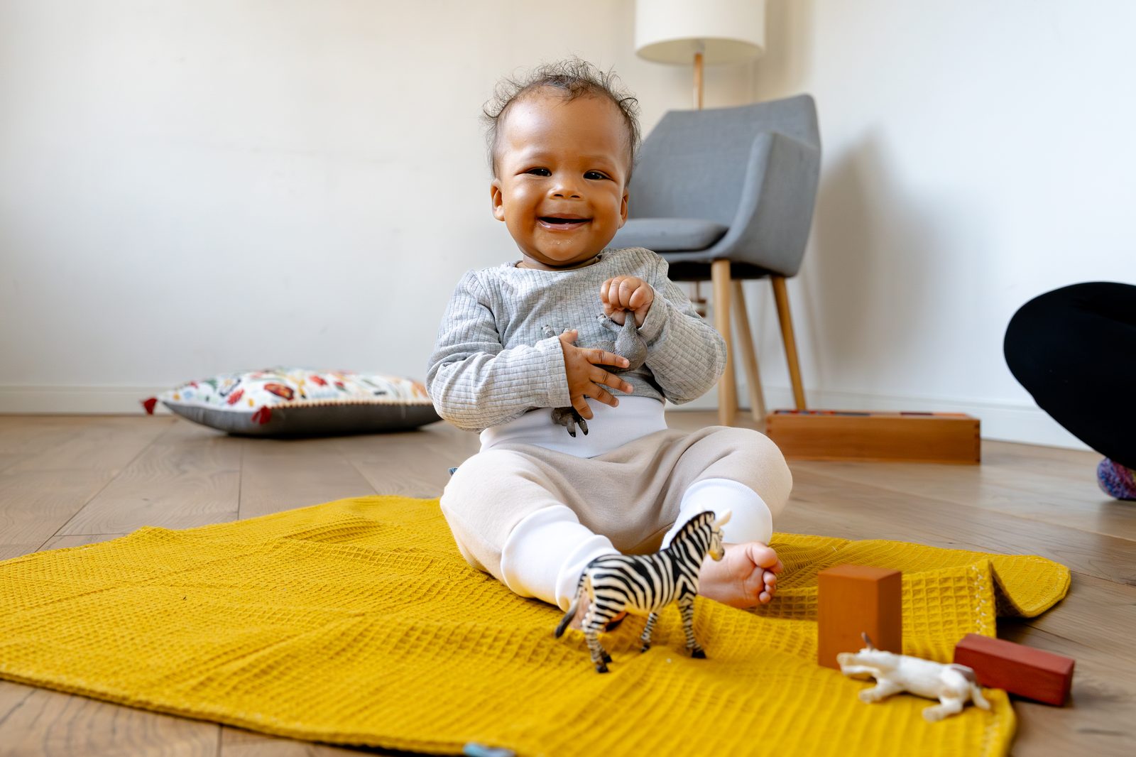 Lächelndes Baby sitzt auf einer Krabbeldecke und spielt mit einem Tierfigur